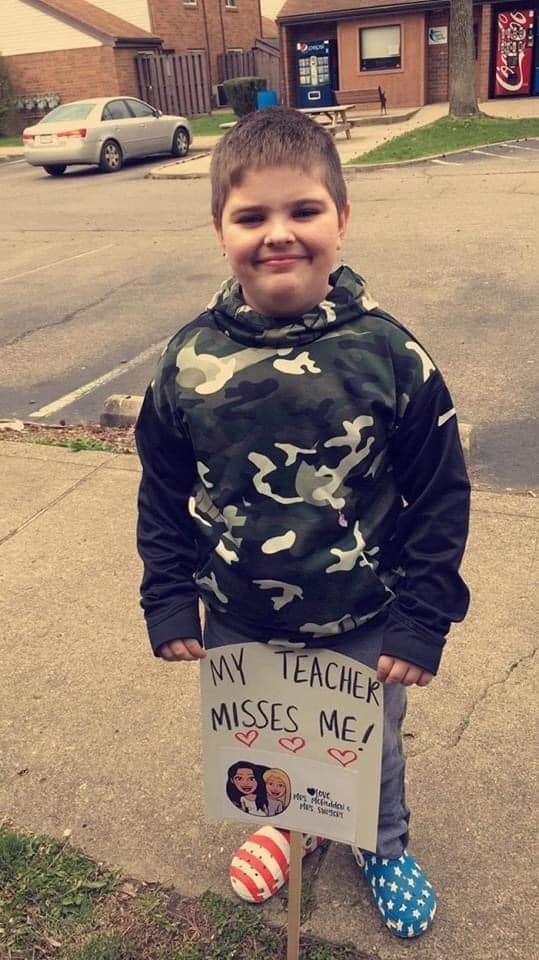 Student posing with sign that says "My teacher misses me!"